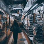 Pessoas circulam e fazem compras em um mercado interno com lojas e produtos expostos.