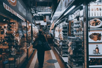 Pessoas circulam e fazem compras em um mercado interno com lojas e produtos expostos.