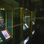 Fileira de máquinas iluminadas de autoatendimento para compra de bilhetes em uma estação de transporte público.