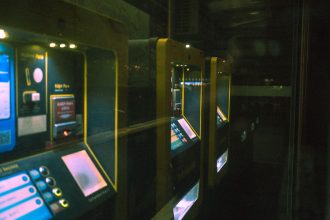 Fileira de máquinas iluminadas de autoatendimento para compra de bilhetes em uma estação de transporte público.