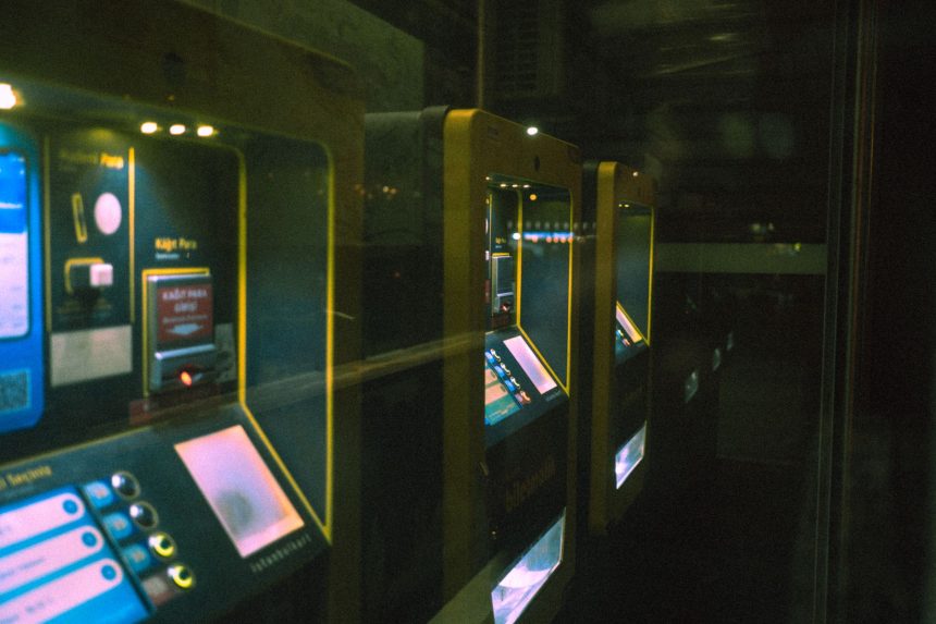Fileira de máquinas iluminadas de autoatendimento para compra de bilhetes em uma estação de transporte público.