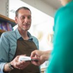 Funcionário de uma loja auxilia um cliente durante uma transação de pagamento.